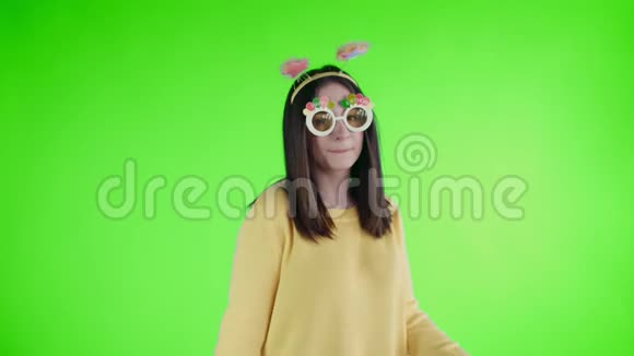 漂亮的年轻女子戴着滑稽的帽子和眼镜独自在绿色的屏幕上跳舞视频的预览图
