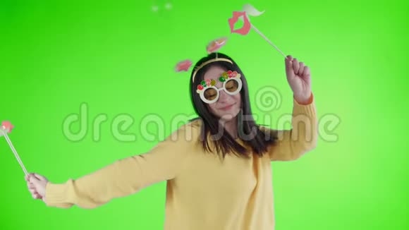 漂亮的年轻女子戴着滑稽的帽子和眼镜独自在绿色的屏幕上跳舞视频的预览图