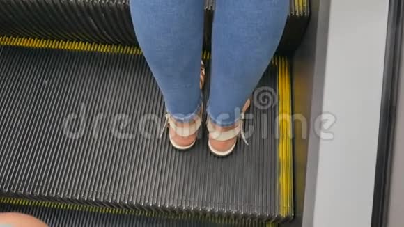 一个穿牛仔裤穿夏季鞋凉鞋的女人的腿在一个移动的扶梯上视频的预览图