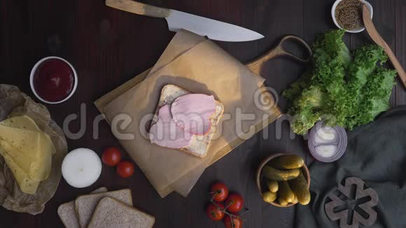 三明治平躺着把火腿片和蔬菜放在木板上放在灯光下厨师的手加了洋葱视频的预览图