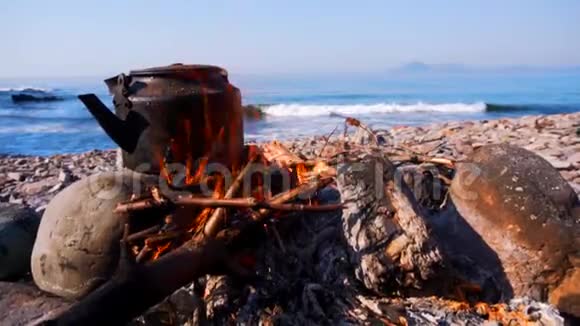 在蔚蓝的大海背景下在岩石海滩上的篝火上点燃水壶视频的预览图