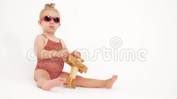 穿着泳衣和太阳镜的婴儿玩普通木制玩具飞机视频的预览图