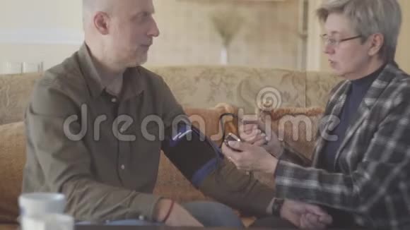 年长夫妇坐在沙发上女人用测压仪测量男人的血压登录未定级视频的预览图
