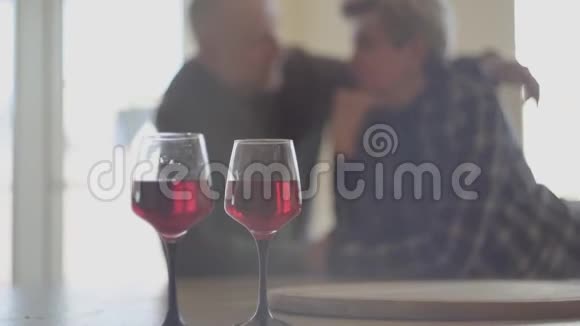 两杯红酒和背景是老年夫妇的剪影男人抱着女人吻她的鼻子Slog视频的预览图
