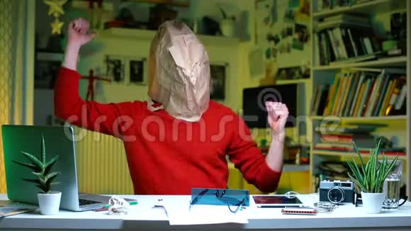 一个头上戴着纸袋的人坐在办公室的一张桌子旁视频的预览图