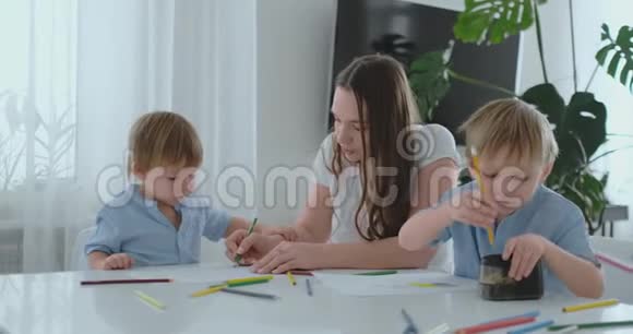 年轻的妈妈和两个儿子24岁的孩子在坐在客厅桌子旁慢动作的博梅加上画铅笔视频的预览图
