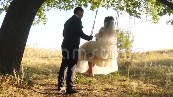 在树枝上的绳子上摆动快乐的年轻家庭蜜月之旅亲爱的夫妇在公园里骑着秋千视频的预览图