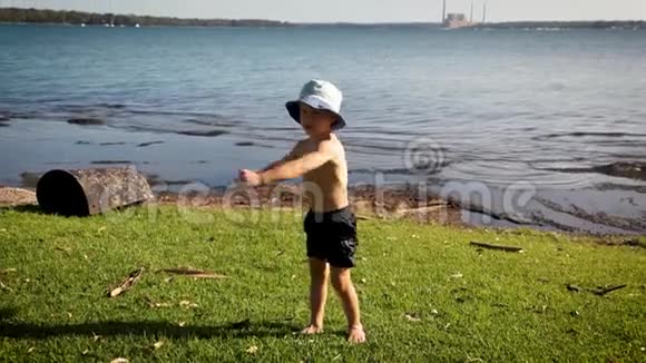 夏天的时候一个穿着短裤戴着斗笠的小男孩在湖边的草地上展示了他对如何做的看法视频的预览图