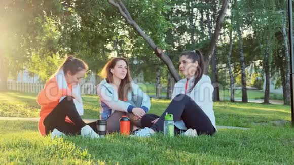 三个女孩的朋友在早上慢跑锻炼后坐在草地上聊天视频的预览图