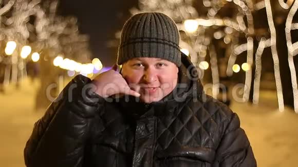 一幅快乐的男人在寒冷的冬夜用手指在户外打电话给我的画像视频的预览图