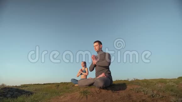 瑜伽疗法运动男女在蓝天背景下一起在山顶上的莲花位置冥想视频的预览图