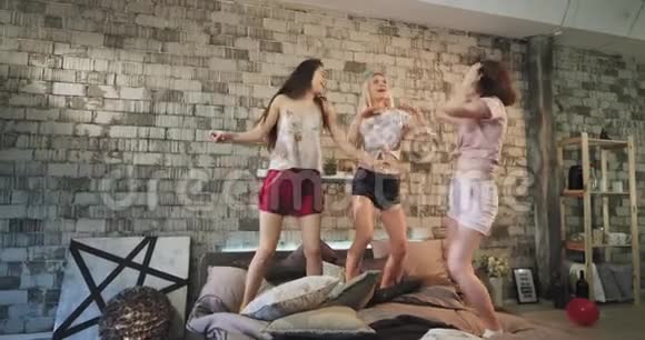 在睡衣派对上跳舞的女士在现代化的城市卧室设计中享受快乐时光跳过床视频的预览图