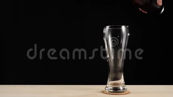 新鲜啤酒在啤酒杯上手把一杯美味的手工啤酒倒入黑色背景的木桌上视频的预览图