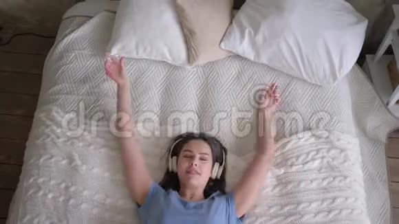 在家里放松的时候喜欢戴耳机的女性会躺在床上听手机里的歌曲和音乐视频的预览图