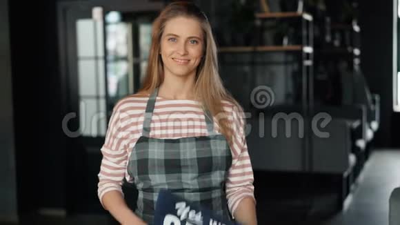 一幅美丽的女孩站在咖啡馆里举着欢迎顾客的开放标志视频的预览图