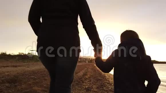 母亲和儿子在黄昏的齐利维海滩散步视频的预览图