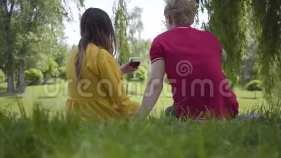 年轻的幸福夫妇喜欢在美丽的花园或公园里用葡萄酒野餐愉快地聊天和微笑视频的预览图