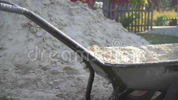 一名工人用铁锹把沙子填到手推车里进行施工铲子和手推车用沙子在车轮上视频的预览图
