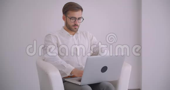 戴着眼镜长着大胡子的白种人成年商人用笔记本电脑坐在扶手椅上的特写镜头视频的预览图