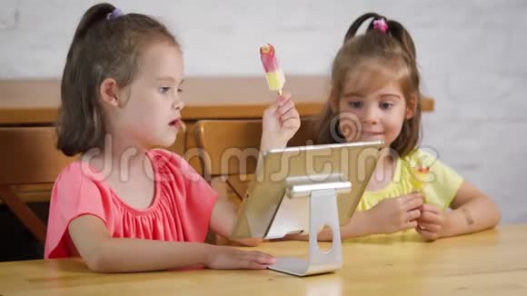 两个小女孩吃冰淇淋看平板电脑上的卡通片视频的预览图