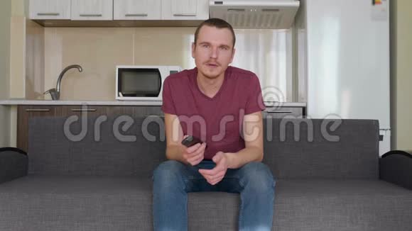 一个男人坐在沙发上换电视频道打哈欠视频的预览图