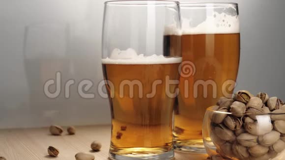 新鲜啤酒两个玻璃杯放着美味的冷啤酒靠近茶托在白色背景的木桌上放一些开心果视频的预览图