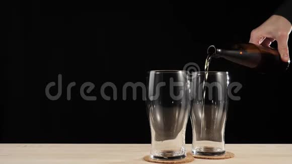 新鲜啤酒在啤酒杯上用手把美味的手工啤酒倒在玻璃里从棕色的瓶子里倒入木桌上与黑色的放在一起视频的预览图