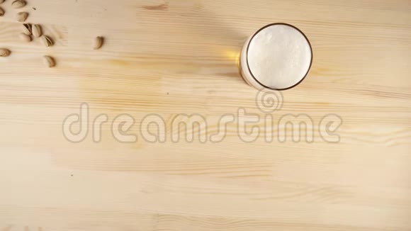 新鲜啤酒一些开心果被扔在玻璃旁边在背景上的木桌上放着冷啤酒冷鲜啤酒视频的预览图