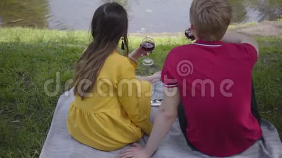 恋爱中的年轻夫妇在美丽的盛开的花园或公园里愉快地聊天和微笑着用葡萄酒野餐日期视频的预览图
