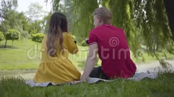年轻的幸福夫妇喜欢在美丽的花园或公园里用葡萄酒野餐愉快地聊天和微笑视频的预览图