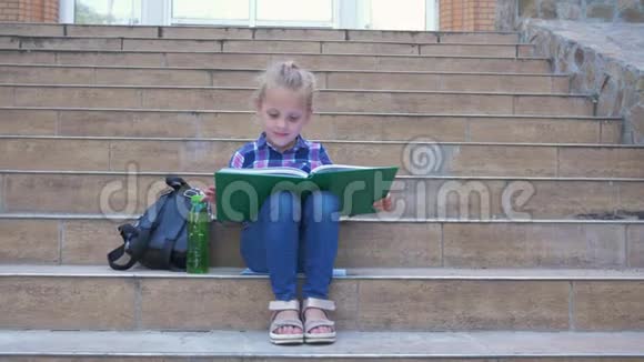 学生小女孩在休息时坐在学校的台阶上挨着背包看书视频的预览图