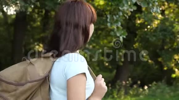 带着背包的女旅行者沿着森林道路行走远足的女人在森林里散步夏天快乐的徒步旅行者女孩视频的预览图