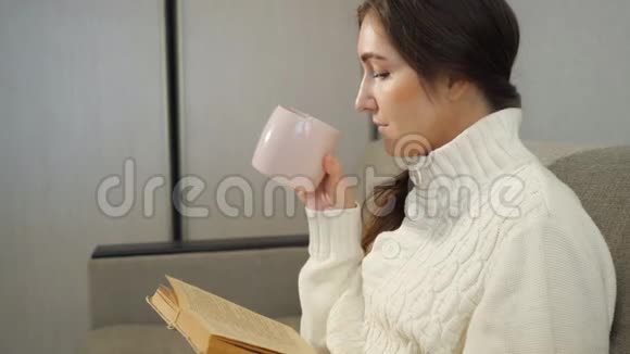 漂亮的女孩在家里的沙发上看书和喝咖啡视频的预览图