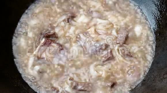 肉片和许多洋葱在肉汤或油中在铸铁锅中煮沸生火做饭传统东方文化视频的预览图