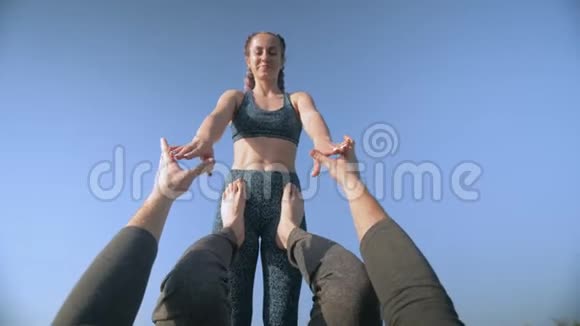 阿克罗瑜伽一个梳着辫子的运动微笑女孩的肖像在天空的背景下着她的男性伴侣的腿视频的预览图