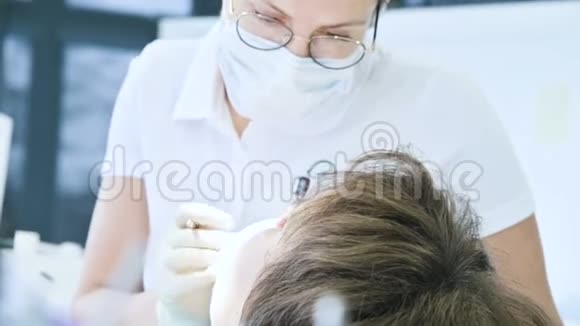 女牙医戴眼镜面罩和白帽检查病人的口腔牙医的工作视频的预览图