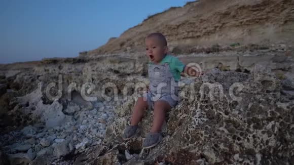 日落时坐在海边的石头上孩子说话坐立不安视频的预览图