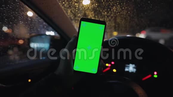 POV晚上在车里用绿色屏幕的男性手握智能手机视频的预览图