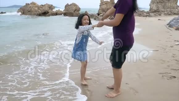 慢动作亚洲小女孩和妈妈一起在沙滩上玩自然海浪海岸暑假概念视频的预览图