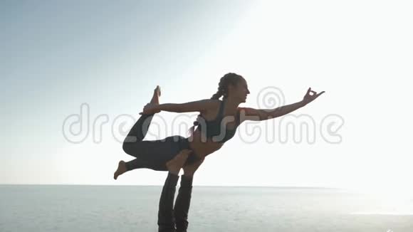 一对在草地上做杂技瑜伽的夫妇穿着运动服的年轻女子正在平衡她的男性伴侣的腿背景是视频的预览图