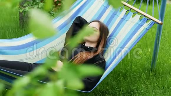 美丽的年轻女子睡在花园里的吊床上休息和打瞌睡视频的预览图