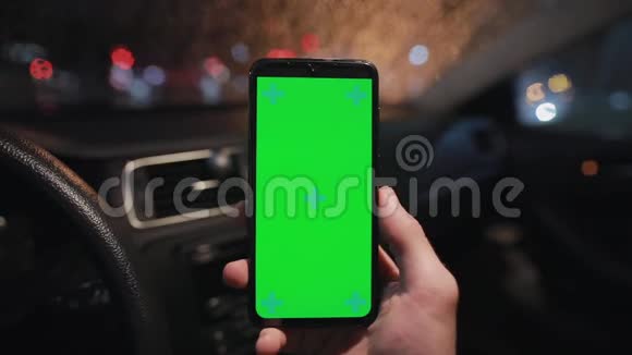 POV晚上在车里用绿色屏幕的男性手握智能手机视频的预览图