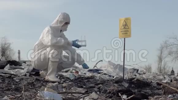 女科学家穿着制服戴着防护手套拿着试管从肮脏的大垃圾场取样垃圾视频的预览图