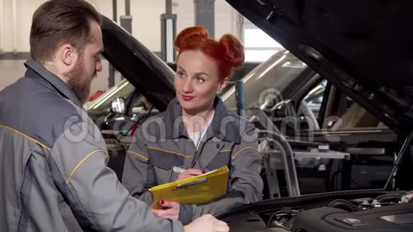 漂亮的女机械师和她的男同事检查一辆汽车的发动机视频的预览图