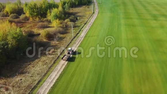 一辆拖拉机沿着一片绿色的田野在公路上行驶初秋农场工作空中镜头视频的预览图