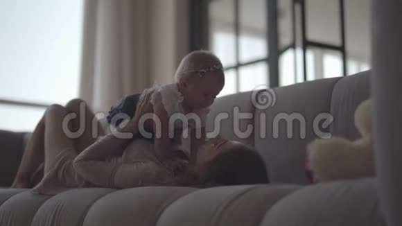 可爱苗条的年轻女人和女婴躺在沙发上母亲在家陪孩子玩幸福的概念视频的预览图