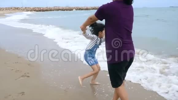 慢动作亚洲小女孩和妈妈一起在沙滩上玩自然海浪海岸暑假概念视频的预览图