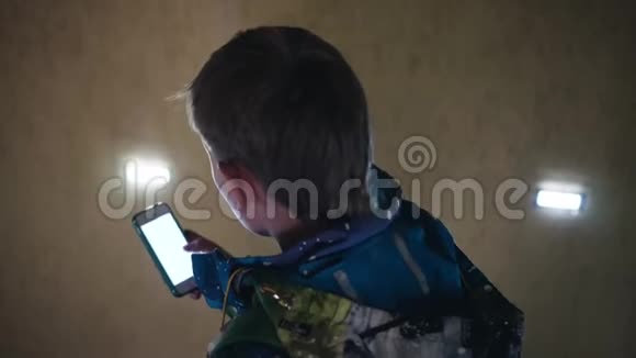 男孩站在楼梯上在你的智能手机上拨一个号码从后面看视频的预览图