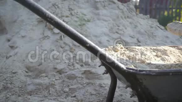 一名工人用铁锹把沙子填到手推车里进行施工铲子和手推车用沙子在车轮上视频的预览图