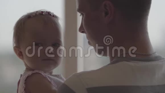 后视的男子抱着小女婴在他怀里窗前特写作为父亲的乐趣爱视频的预览图
